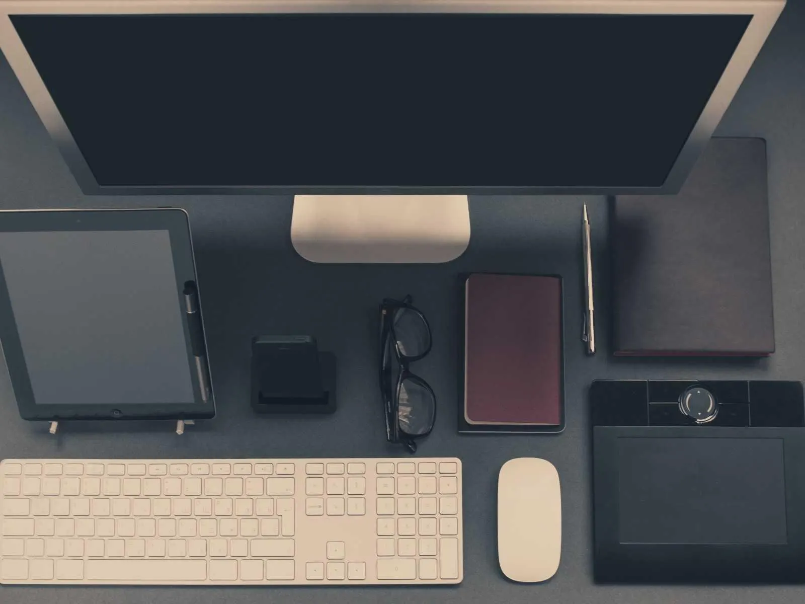 Neatly arranged desk with monitor, keyboard, tablet and notebooks